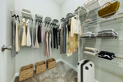 A white closet with clothes hanging and baskets on the floor.