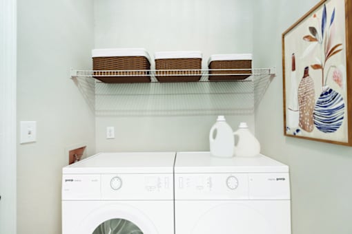 A white front loading washing machine with a shelf above it.