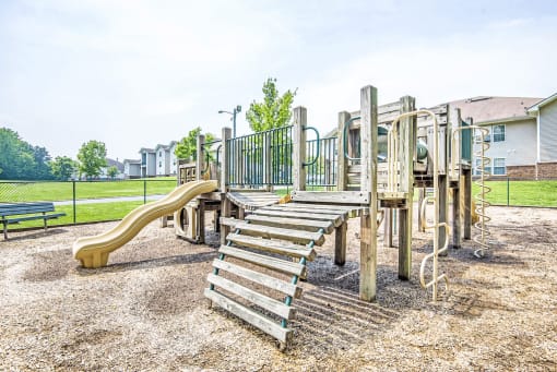 Wooden Playground with Yellow and Green Accents on Mulch with Bench and Fence