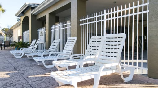 White pool lounge chairs on sun deck surrounded by white metal fence