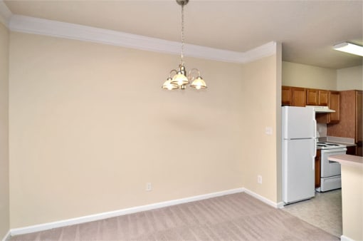 Dining room area with carpet throughout. Chandelier is overhead with kitchen on the right side.