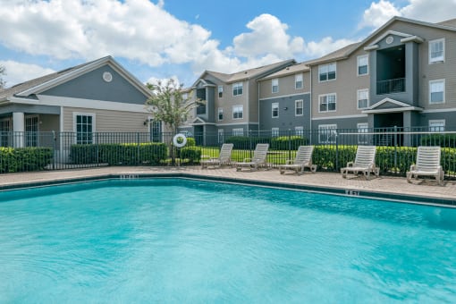 Swimming pool with lounge seating and apartment building exterior in the background