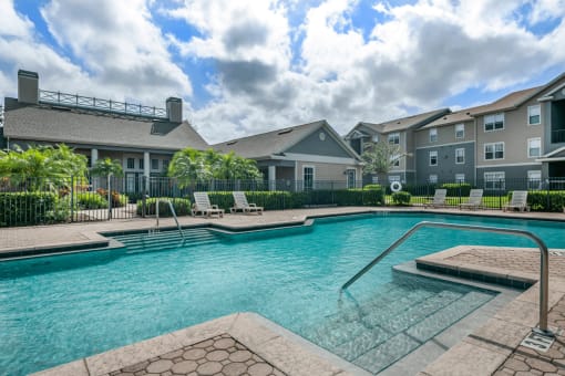 Swimming pool with lounge seating surrounded by native landscaping and apartment building exterior in the background