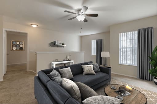 Virtually staged living room with tan carpeted flooring, two large windows with white vertical blinds, a white multi-speed ceiling fan, couch, and coffee table