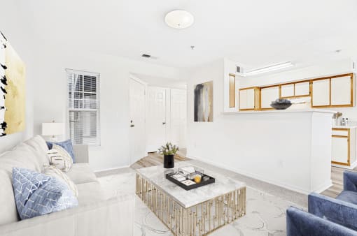 Virtually staged carpeted living room with grey couch and accent chairs with coffee table and modern artwork. Kitchen and dining room in background