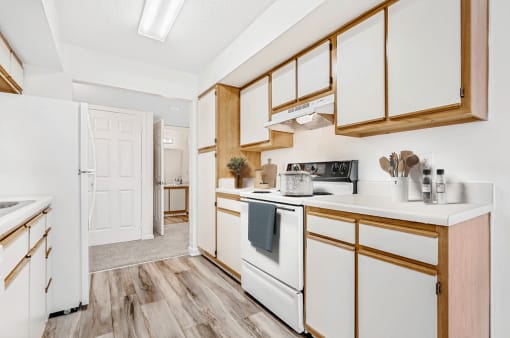 Virtually staged; Kitchen with wood floors, white appliances, and wood cabinets. Guest bathroom in background. Kitchen accessories displayed
