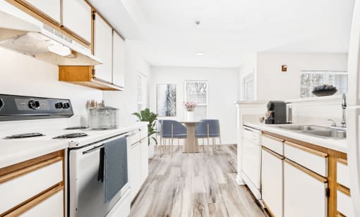 Virtually staged; Kitchen with wood floors, white appliances, and wood cabinets. Kitchen accessories and dining table in background with blue accent chairs