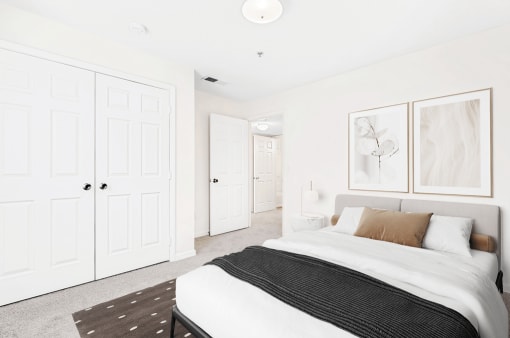 Virtually staged; Carpeted bedroom looking towards hallway with closet in background. Bed and side tables with grey/tan accents and wall art