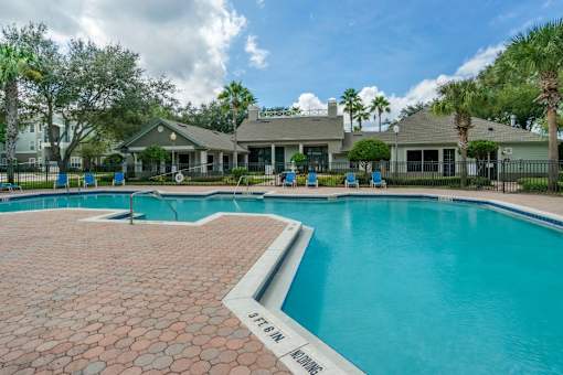 Swimming pool with sundeck, lounge seating, with clubhouse in the background surrounded by landscaping