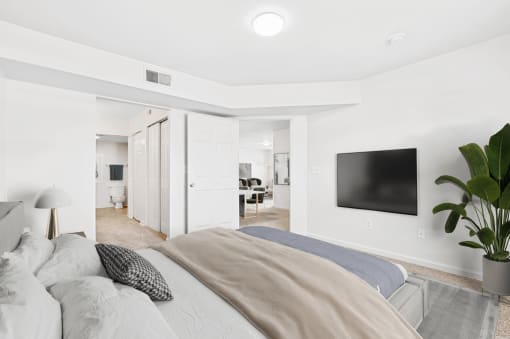 Virtually staged bedroom. Carpeted bedroom with grey and tan accent bed/artwork. Closet and bathroom in background.