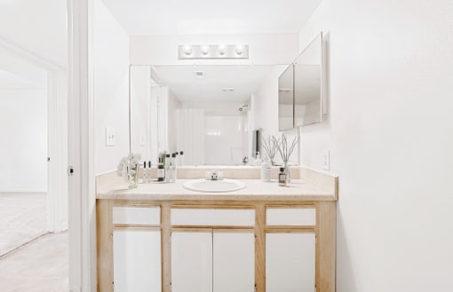 Virtually staged bathroom with tile flooring, wood cabinets, and white counters. Grey accent mirror and toiletries.