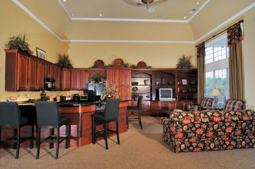 Resident clubhouse with ample seating. Cabinets line the back wall with bar stools surrounding the bar top table.