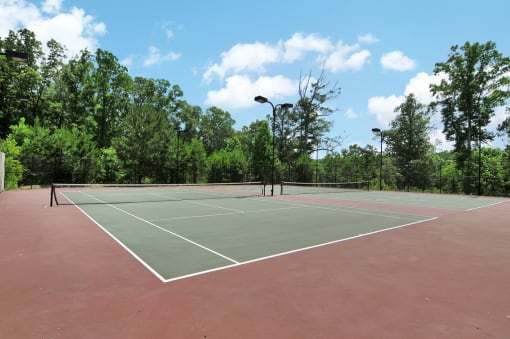 Community tennis courts with a red base and green courts with lines. A black fence surrounds the courts.