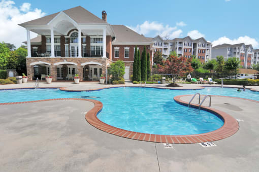 Community pool with pool furniture throughout. The clubhouse is in the background, surrounded by trees.