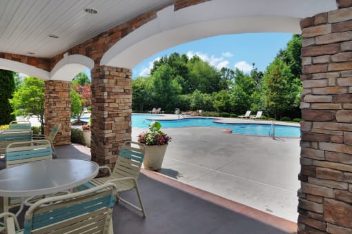Pool deck seating area covered by clubhouse balcony above. Tables and chairs are on both sides of the covered area.