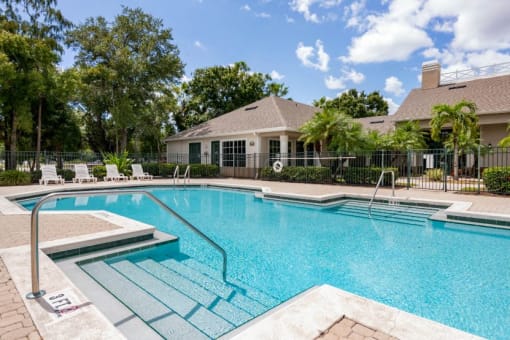 Leasing Office Exterior with Swimming Pool and Sun Deck with Lounge Chairs with Trees and Building Exteriors in the Background