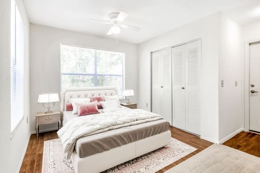 A study staged as a bedroom with hardwood flooring, a ceiling fan, window, and view of laundry room’s bifold doors