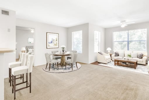 Staged living room with a dining room with hardwood-style flooring and carpet combo, a ceiling fan, and several windows with window blinds.