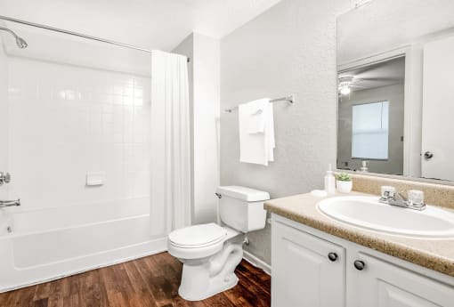 Staged bathroom with hardwood-style floors, a shower/tub combo with tile surround, a single sink vanity with laminate countertops, and white cabinets.