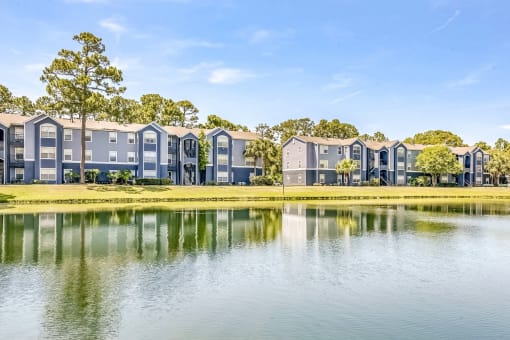 Two three-story apartment buildings along the waterfront, lined with grass and trees.