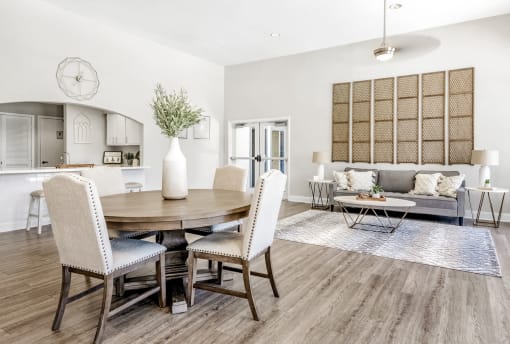 Lounge area with hardwood-style floors, a sofa with two side tables and a coffee table, a round dining table with four chairs, and a pass-thru to a kitchen with two barstools.