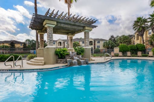 Swimming pool with sundeck surrounded by native landscaping and apartment building exterior in the background