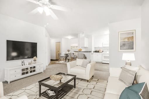 Virtually staged living room with carpet, accent rug, ceiling fan with light, white couch and chair, wall mounted television with kitchen and dining area in the background
