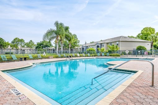 Swimming pool with a brick paver sundeck, palm trees, and lounge chairs.