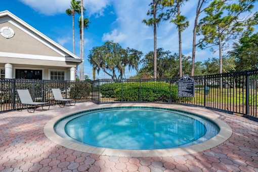 Fenced in Wading Pool with Lounge Chairs with Leasing Office Exterior and Trees in the Background