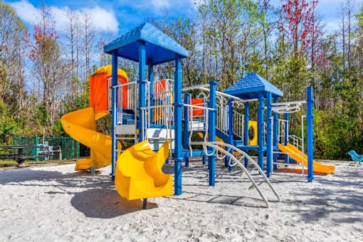 Blue and Yellow Playground on Sand with Building Exterior and Trees in the Background
