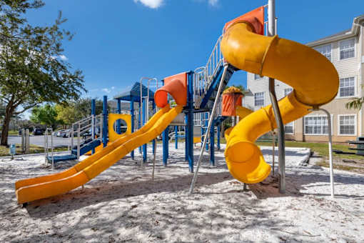 Blue and Yellow Playground on Sand with Building Exterior and Trees in the Background