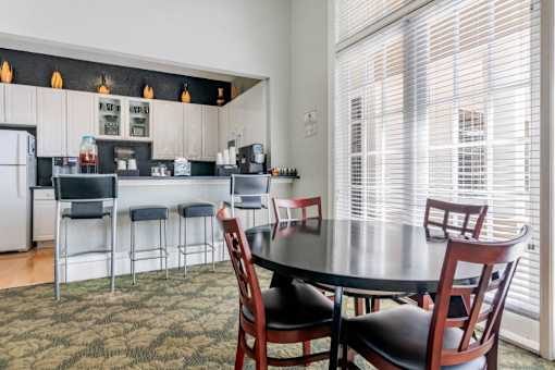 Clubhouse Seating Area with Dining Room Tables in Front of Clubhouse Kitchen Bar with Barstools with Refreshments and Coffee on the Bar in Front of White Cabinets
