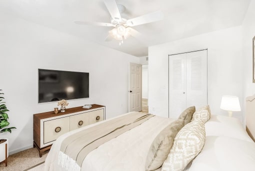 A staged bedroom with carpet, and a ceiling fan, window. Full bed with tufted headboard on top of a rug and art above the bed.
