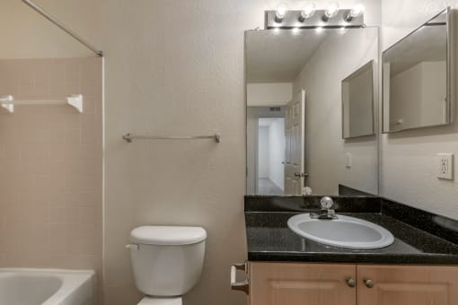 Bathroom with Blonde Cabinets, Black Counters and White Bathtub and Beige Shower