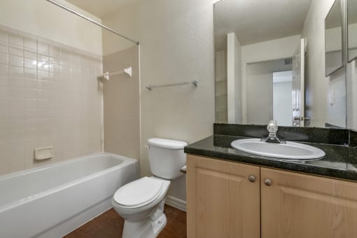 Bathroom with Blonde Cabinets, Black Counters and White Bathtub and Beige Shower