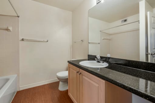 Bathroom with Blonde Cabinets, Black Counters and White Bathtub and Beige Shower