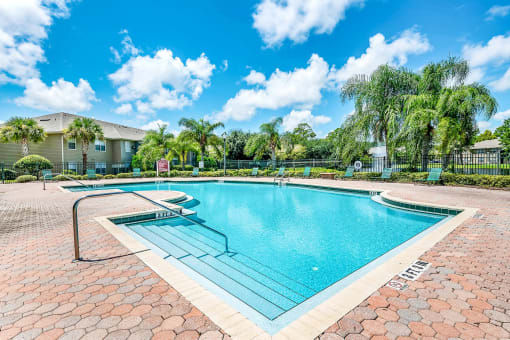 Swimming pool with a brick paver sundeck, palm trees, and lounge chairs.