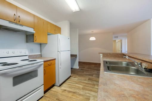 Kitchen with Wood Cabinets, Tan Counters and white Appliances, with view of dining room and built in desk in the background