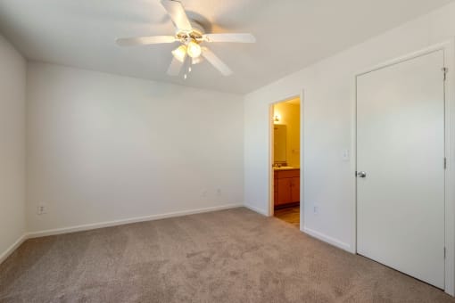 Carpeted Bedroom with white walls and ceiling fan, with view of bathroom