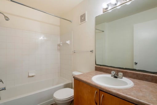 Bathroom with wood flooring, toilet, shower tub combo with tile back splash, towel bar, brown cabinets