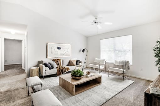 Staged living room with carpeted flooring, a ceiling fan, couch, chairs, coffee table, and art on the wall.