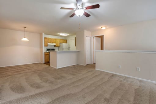 Spacious living room with carpet flooring, multi speed ceiling fan, dining room with pendant lighting, and kitchen in the background