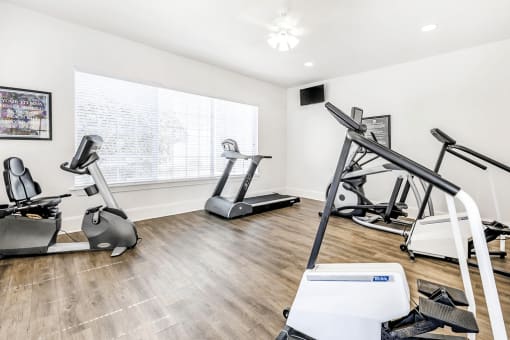 Fitness center with cardio machines and large window with wall mounted television and ceiling fan with light