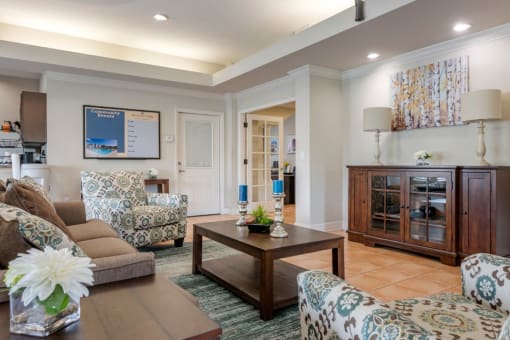 Clubhouse lounge with couch, chairs, coffee table, wall art, tile flooring, and rug