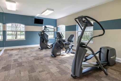 Fitness center with cardio equipment, wall mounted television, and large mirror for natural lighting