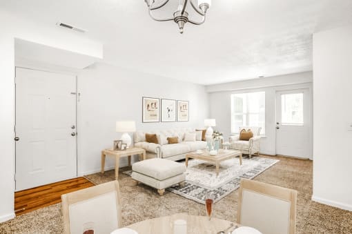 The entry door of the apartment on the left side of the room gives way to a hardwood-style landing and a spacious living area. The remaining flooring throughout the space features tan carpet.