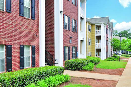 A row of red brick apartment buildings with green bushes in front.