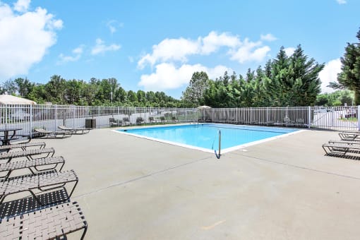 a swimming pool with chaise lounge chairs and trees in the background
