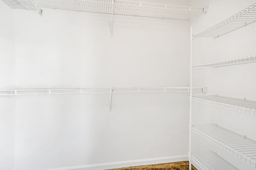 a walk in closet with white shelving and white walls