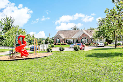 A playground with a red slide in the foreground and a house in the background.